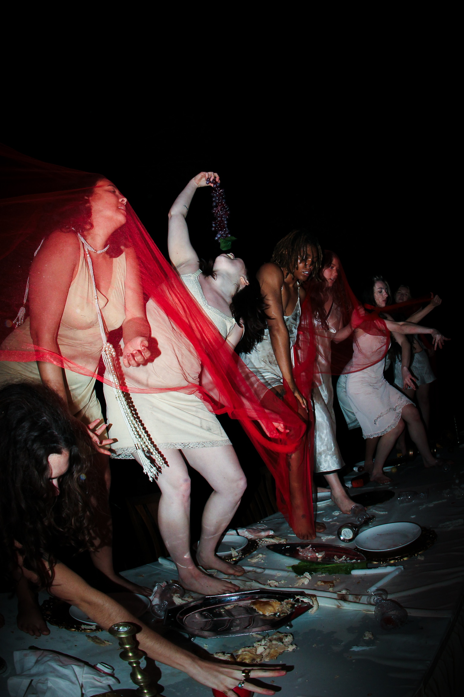 Dancers in slips moving across the ruined banquet table at night